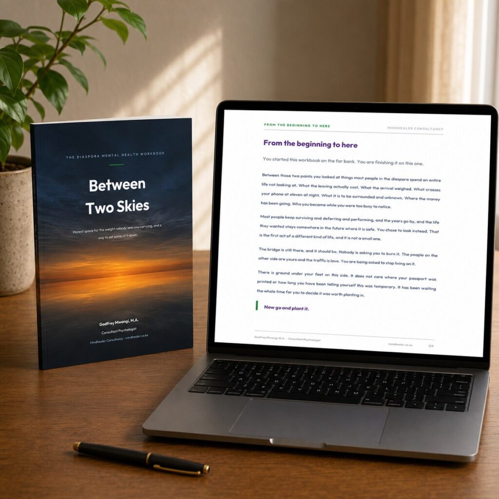 Between Two Skies diaspora mental health workbook in print beside the fillable PDF open on a laptop